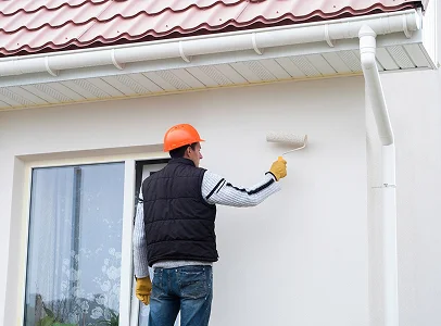 Un ouvrier portant un casque orange peint le mur extérieur d'une maison avec un rouleau à Argy près de Châteauroux dans l'Indre 36